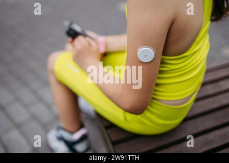 Ein Mädchen mit Diabetes überprüft ihren Blutzuckerspiegel an einer Insulinpumpe, trägt einen CGM-Sensor Stockfoto