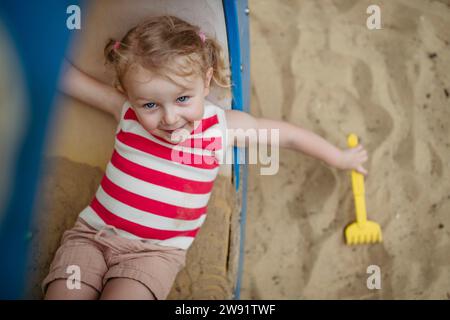 Glückliches kleines Mädchen mit Spielzeugarke, das auf dem Spielplatz im Klettergerüst liegt Stockfoto