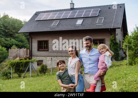 Glückliche Familie steht vor ihrem Familienhaus mit Solarpaneelen auf dem Dach Stockfoto