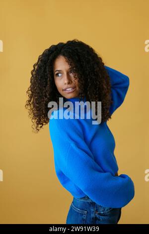 Frau mit lockigem Haar, die blauen Pullover auf gelbem Hintergrund trägt Stockfoto