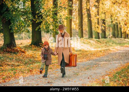 Mutter hält Hände mit dem Sohn und läuft im Herbstpark Stockfoto