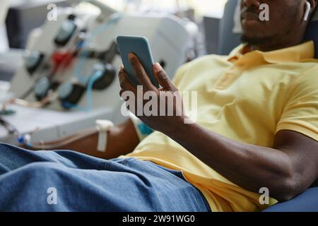 Hand eines Mannes, der ein Handy in der Blutspendeeinrichtung hält Stockfoto