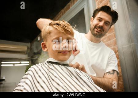 Lächelnder Friseur, der im Salon die Haare des Kunden putzt Stockfoto