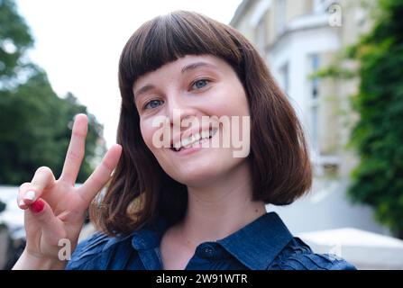 Glückliche junge Frau gestikuliert Friedenszeichen Stockfoto