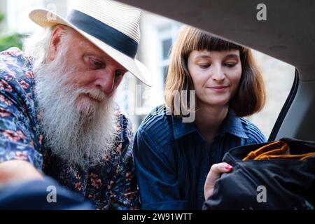 Lächelnde junge Frau mit Vater, der Rucksäcke in den Kofferraum steckt Stockfoto