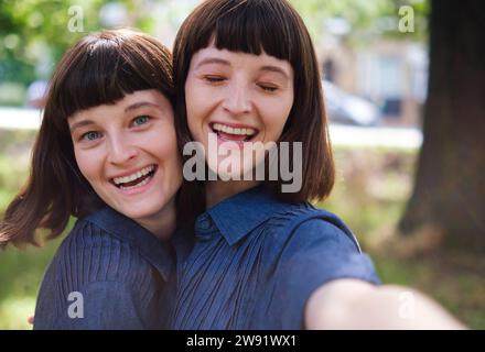 Fröhliche Zwillingsschwestern machen Selfie im Park Stockfoto