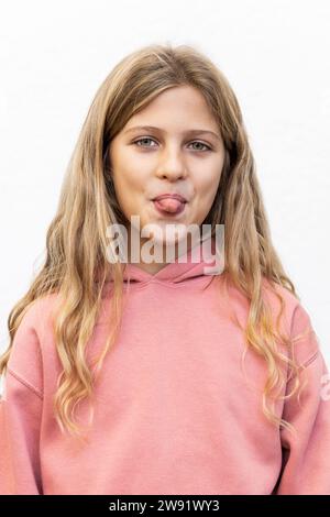 Verspieltes blondes Mädchen, das die Zunge vor weißem Hintergrund ausragt Stockfoto