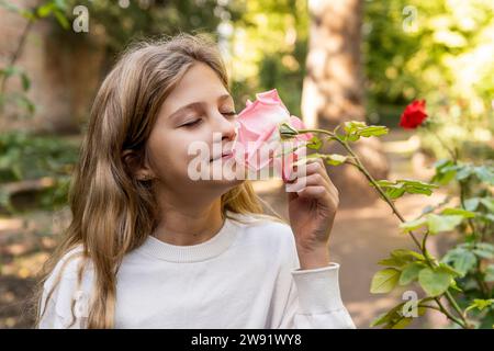 Lächelndes Mädchen, das rosa Rosenblume im Park riecht Stockfoto