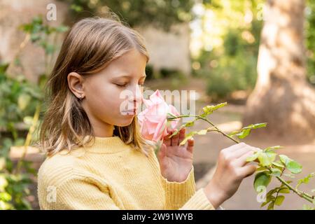 Mädchen mit geschlossenen Augen riecht rosa Rosenblume im Park Stockfoto