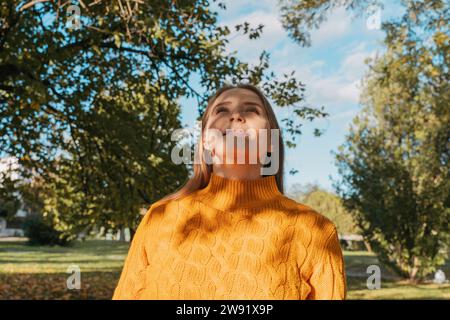 Lächelnde Frau mit orangefarbenem Pullover im Herbstpark Stockfoto