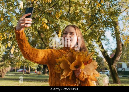 Glückliche Frau mit Ahornblättern und Selfie im Herbstpark Stockfoto