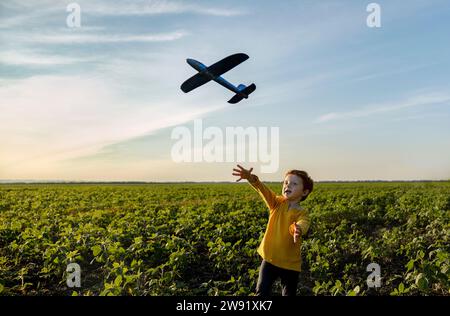 Sorgloser Junge, der mit Spielzeugflugzeugen auf dem Ackerfeld unter dem Himmel spielt Stockfoto