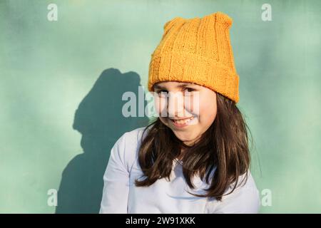 Lächelndes Mädchen mit Strickmütze vor der grünen Wand Stockfoto