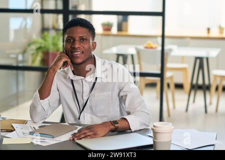 Ein lächelnder junger Geschäftsmann sitzt mit Dokumenten am Schreibtisch Stockfoto