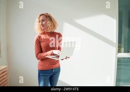 Lächelnde Geschäftsfrau, die mit einem Laptop im Büro steht Stockfoto