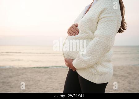 Schwangere Frau, die am Strand mit Händen auf dem Bauch steht Stockfoto