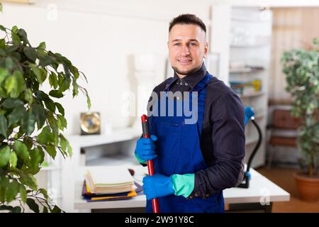 Männlicher professioneller Hausmeister, der im Büroinneren Staub staubt Stockfoto
