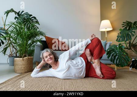 Lächelnde Frau, die Yoga macht, liegend auf dem Teppich zu Hause Stockfoto