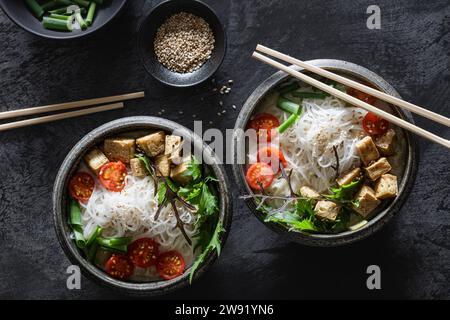 Schüsseln mit veganer Tom-Kha-Kai-Suppe mit Tofu, Tomaten, Salat, Reisnudeln, Sesamsamen und Zwiebeln Stockfoto