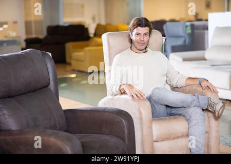 Männlicher Möbelverkäufer präsentiert Sessel zum Verkauf im Möbelausstellungsraum Stockfoto