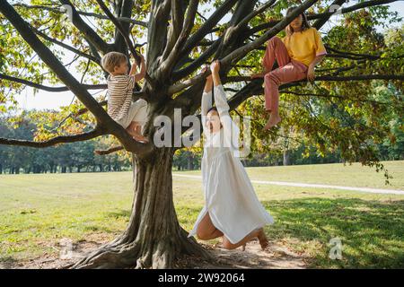 Junge und Mädchen mit Mutter, die an einem Baum im Park hängt Stockfoto