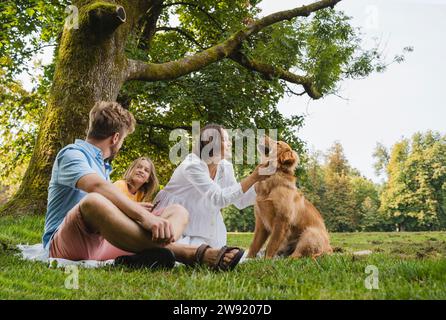 Familie genießt ein Wochenende mit Hund, der im Park auf Gras sitzt Stockfoto