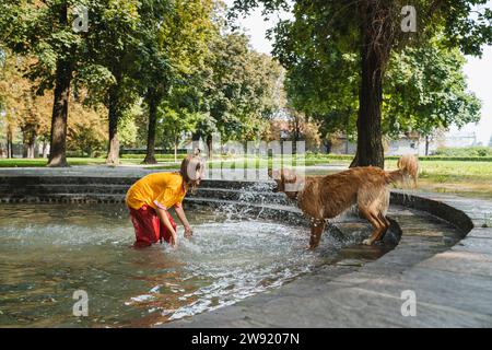 Mädchen spritzt Wasser auf Hund im Brunnen im Park Stockfoto