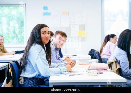 Lächelnde, vielfältige Freunde sitzen am Schreibtisch mit Büchern im Klassenzimmer Stockfoto