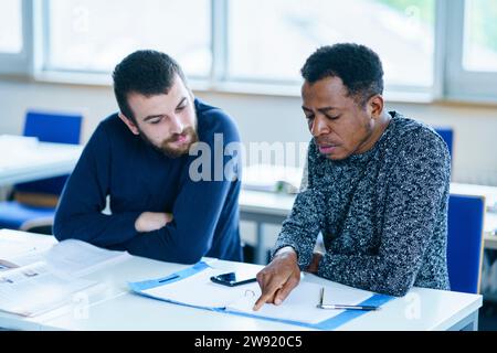 Der Schüler erklärt seinem Freund Notizen am Schreibtisch im Klassenzimmer Stockfoto