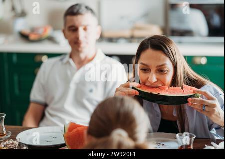 Eine Frau isst eine Scheibe Wassermelone mit der Familie am Tisch Stockfoto