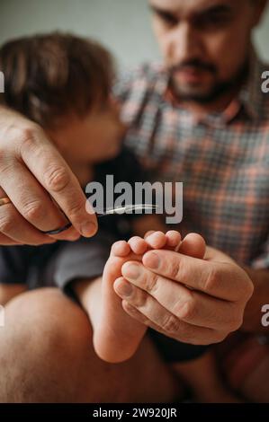 Vater schneidet dem kleinen Jungen die Zehennägel mit einer Schere zu Hause Stockfoto