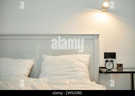 Schlafzimmer innen, Bett mit weißer Bettwäsche und Nachttisch mit Wecker darauf Stockfoto