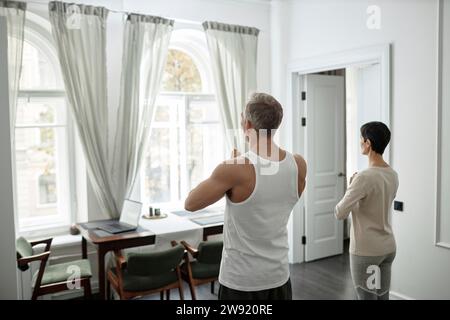 Rückansicht eines adulten Paares, das vor ihnen während der Morgenmeditation zu Hause Palmen faltet Stockfoto