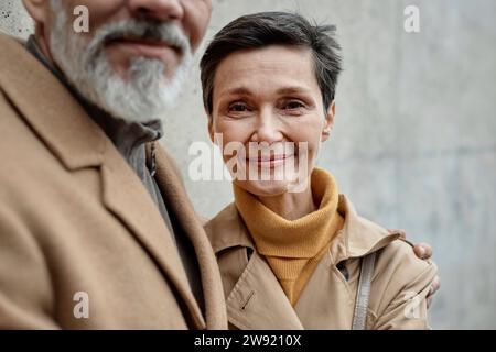 Erwachsene Frau, die in die Kamera neben ihrem Mann mit grauem Bart im Freien steht Stockfoto