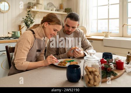 Lächelnde Frau, die Kekse mit Mann am Tisch in der Küche dekoriert Stockfoto