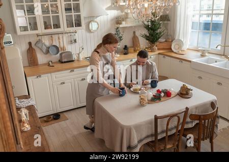 Mann, der Kekse dekoriert, mit Frau, die in der Küche einen Becher hält Stockfoto