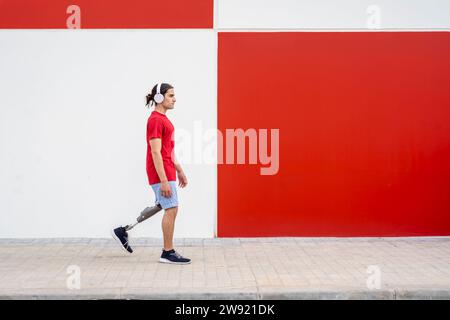 Mann mit schnurlosen Kopfhörern und Gehen mit einer Beinprothese in der Nähe der Wand Stockfoto