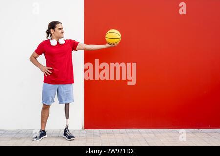 Glücklicher Mann mit einer Beinprothese, der gelben Basketball in der Nähe der Wand hält Stockfoto