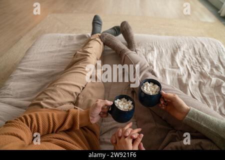 Ein Paar hält zu Hause Tassen mit heißer Schokolade und Marshmallows auf dem Bett Stockfoto