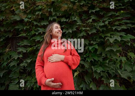 Glückliche schwangere Frau, die den Magen vor Pflanzen berührt Stockfoto