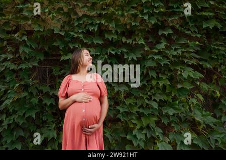 Lächelnde schwangere Frau im Kleid und vor Pflanzen stehend Stockfoto