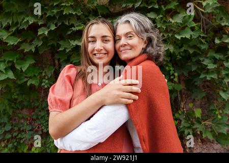 Glückliche Mutter, die schwangere Tochter in der Nähe von Pflanzen umarmt Stockfoto