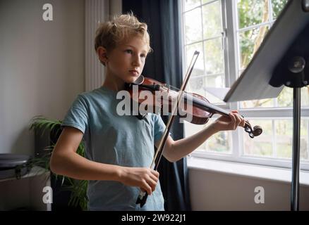 Grundjunge, der zu Hause in der Nähe des Fensters Geige spielt Stockfoto