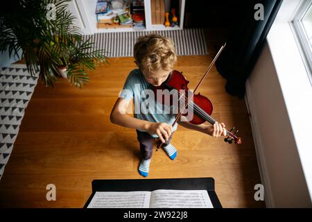 Junge mit blonden Haaren, der zu Hause vor Noten Geige übt Stockfoto