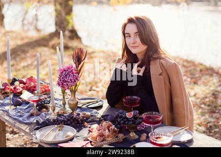 Frau im Mantel und sitzt am Tisch für Thanksgiving im Wald Stockfoto