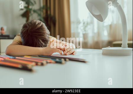 Trauriger Junge, der zu Hause den Kopf auf den Schreibtisch lehnt Stockfoto