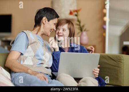 Glückliche Mutter und ihre Tochter mit Behinderung halten einen Laptop zu Hause Stockfoto