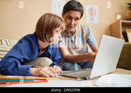 Mutter erklärt der Tochter mit Down-Syndrom zu Hause die Lektion auf dem Laptop Stockfoto