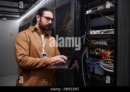 Junger IT-Ingenieur, der Laptop nutzt und ein Computernetzwerk im Datenraum einrichtet Stockfoto