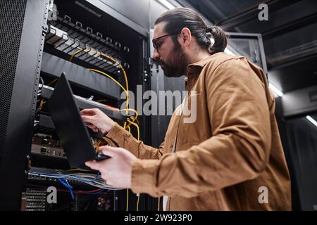 Professionelle IT-Mitarbeiter, die Kabel anschließen und den Laptop im Serverraum halten Stockfoto
